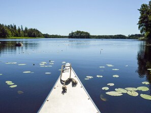 A boat docked on calm water with lily pads, surrounded by trees and a clear sky. - 4 Star Holiday Home in Skattungbyn Orsa (Orsa)
