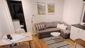 A compact living space with a sofa, a small dining table, a kitchen area, and a single chair. - 4 Star Holiday Home in Skattungbyn Orsa (Orsa)
