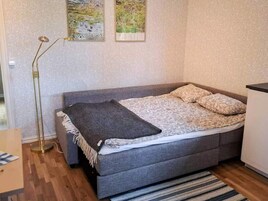 Una cama individual con cabecera gris, una mesita de noche, una lámpara de pie y dos cuadros enmarcados en la pared.