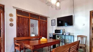 Un comedor con una mesa de madera y bancos, un televisor montado en la pared y una zona de cocina con microondas y refrigerador.
