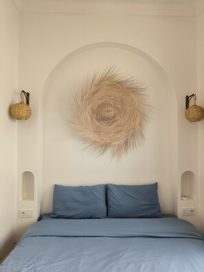 A bedroom with a bed, a wall-mounted circular woven artwork, and two wall-mounted baskets. - Riad 3 rooms, medina, Top Location (Marrakech)