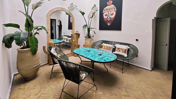 A room with a mirrored wall, a round table with chairs, a sofa with pillows, and large potted plants. - Riad 3 rooms, medina, Top Location (Marrakech)