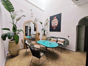Ein Zimmer mit einem Spiegel, einem runden Tisch mit Stühlen, einer Couch mit Kissen und großen Topfpflanzen.