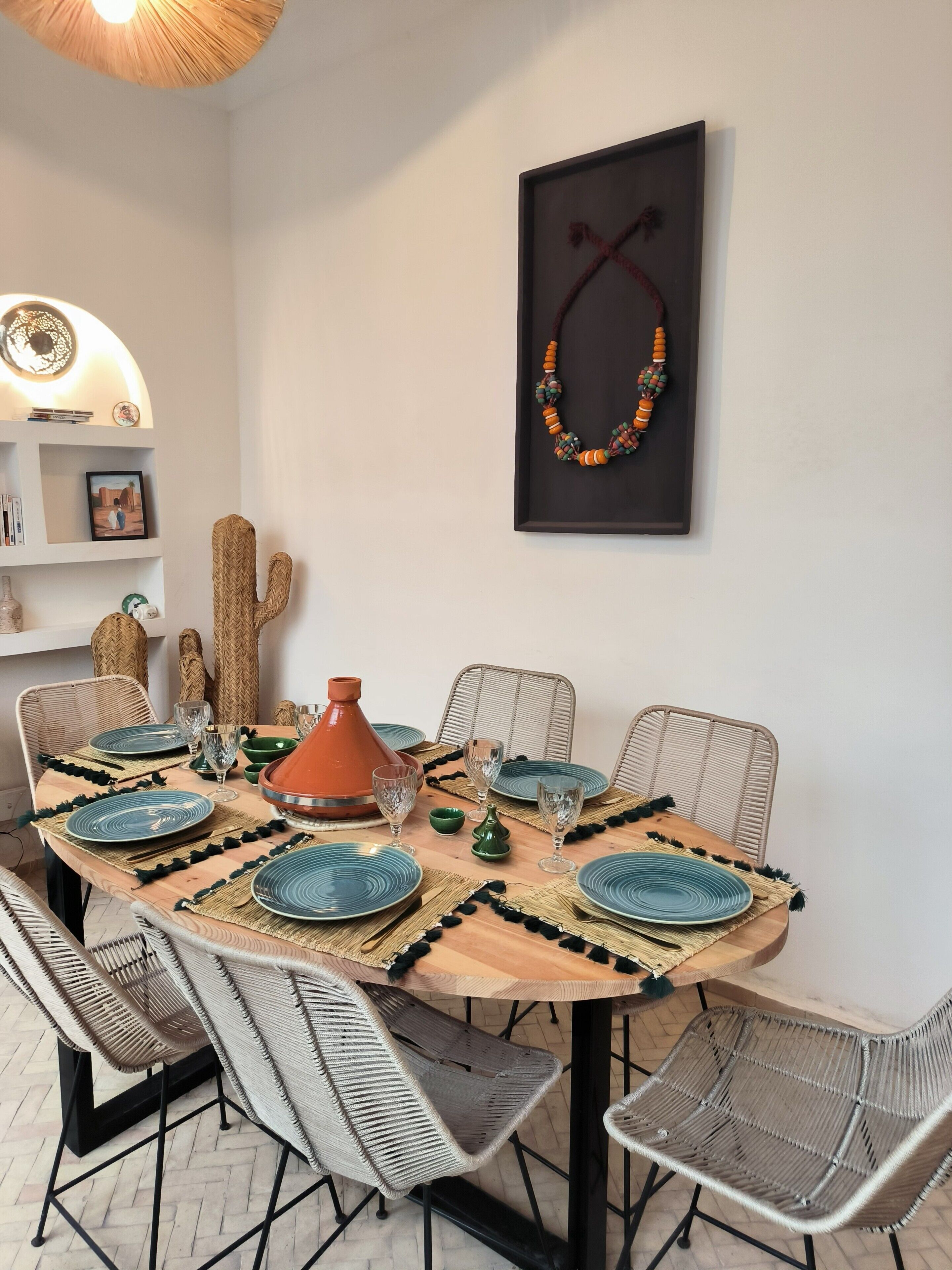 A dining area with a round table, woven chairs, and a Moroccan tagine.