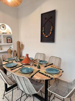 A dining area with a round table, woven chairs, and a Moroccan tagine. - Riad 3 rooms, medina, Top Location (Marrakech)