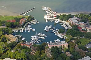 Ein Luftbild eines Yachthafens mit vertäuten Booten, einem Leuchtturm und umliegenden Wohngebäuden.
