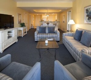 Ein Wohnzimmer mit einer Couch, Sesseln, einem Couchtisch, einem Fernseher und einem Essbereich mit Stühlen und Tisch.
