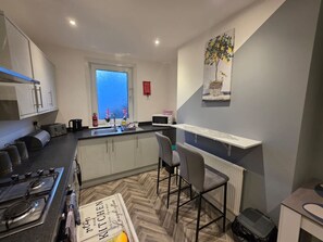 A modern kitchen with a gas stove, microwave, and a window with a view. - Park Place 3 Bedroom House (North Northamptonshire)