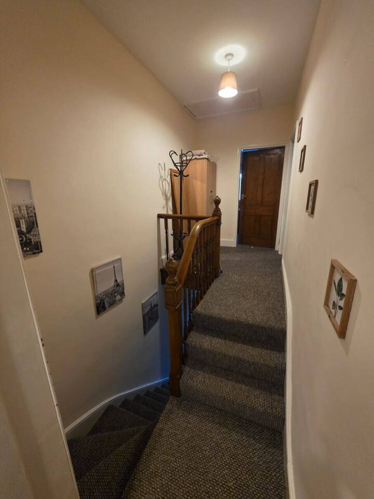 A carpeted hallway with a wooden railing, a coat rack, and framed pictures on the walls.