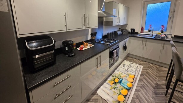 A modern kitchen with grey cabinets, a black countertop, and a window with a view. - Park Place 3 Bedroom House (North Northamptonshire)