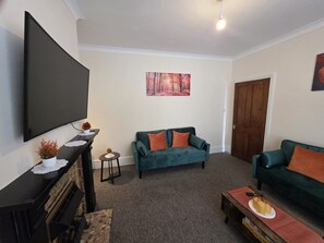 A living room with a flat-screen TV, two sofas, a coffee table, and a fireplace. - Park Place 3 Bedroom House (North Northamptonshire)