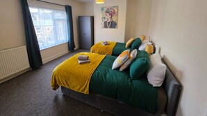 A hotel room with a bed, a window with curtains, a radiator, and a painting on the wall. - Park Place 3 Bedroom House (North Northamptonshire)