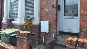 A brick house with a white front door, a bay window, and a green bin outside. - Park Place 3 Bedroom House (North Northamptonshire)