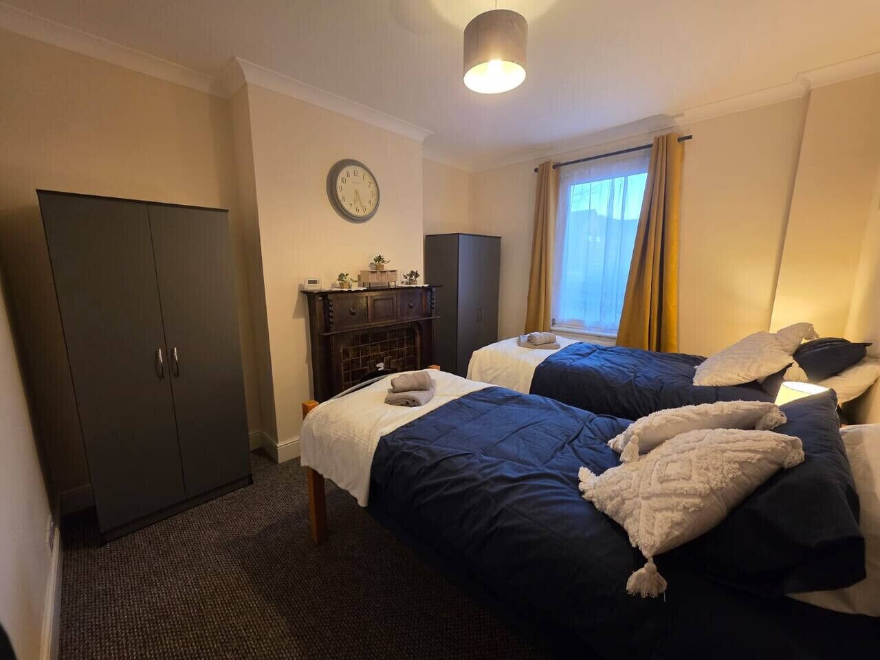 Une chambre d’hôtel avec deux lits, une armoire, une horloge et une fenêtre avec des rideaux.