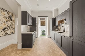A modern kitchen with dark cabinetry, a marble countertop, and a herringbone floor pattern. - The Oakley Residence - Garden View Apartment (1) (London)