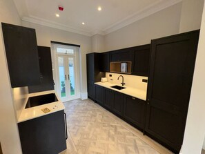 A modern kitchen with dark cabinetry, a white countertop, and a built-in sink. - The Oakley Residence - Garden View Apartment (1) (London)