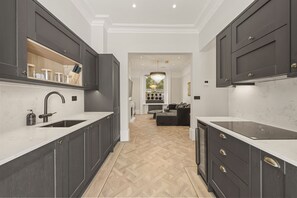 A modern kitchen with dark cabinetry, white countertops, and a herringbone wood floor. - The Oakley Residence - Garden View Apartment (1) (London)