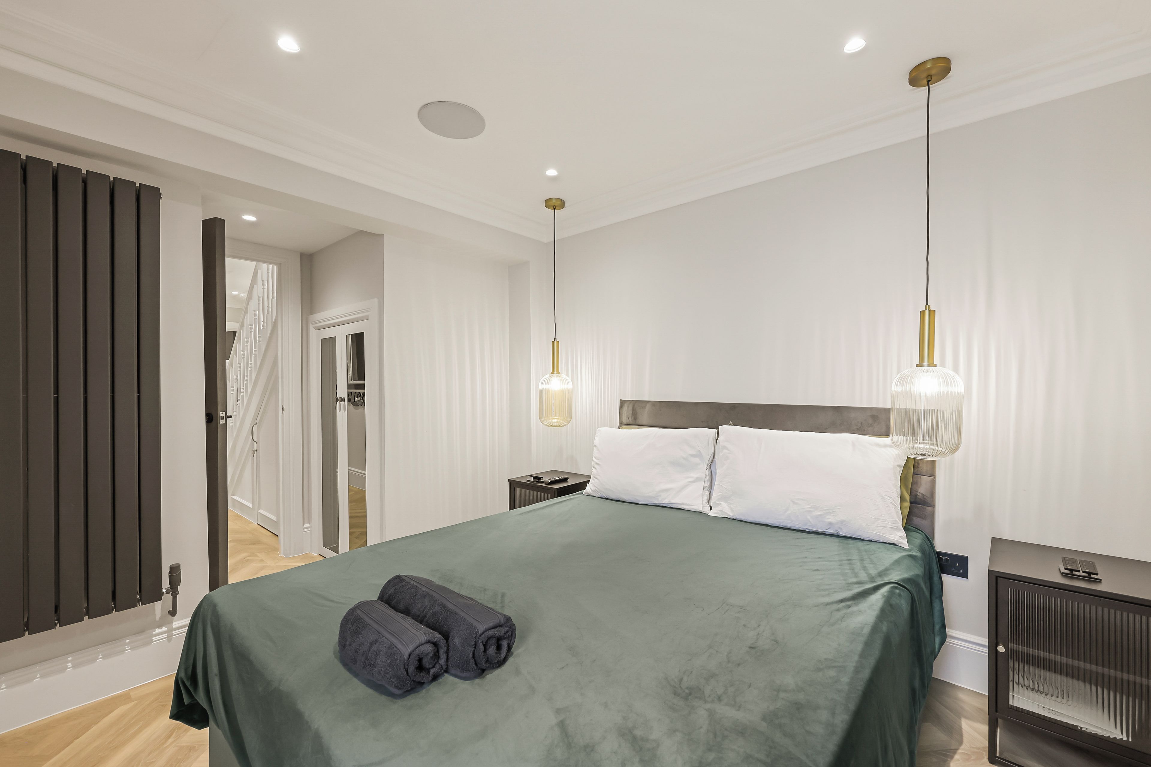 A modern hotel room with a large bed, two bedside lamps, a bedside table, and a view of the hallway.
