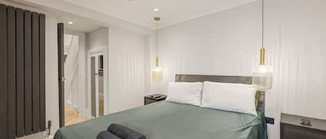 A modern hotel room with a large bed, two bedside lamps, a bedside table, and a view of the hallway.