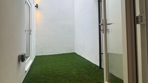 En smal gang med kunstgræs, hvide vægge og en dør, der fører til et lysere område.