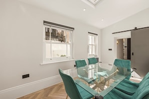 A modern conference room with a glass table and teal chairs, large windows with blinds, and a visible door to another room. - The Oakley Residence - Garden View Apartment (1) (London)