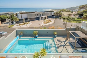 Ein Pool auf dem Dach mit Blick aufs Meer, umgeben von modernen Gebäuden und Grünpflanzen.