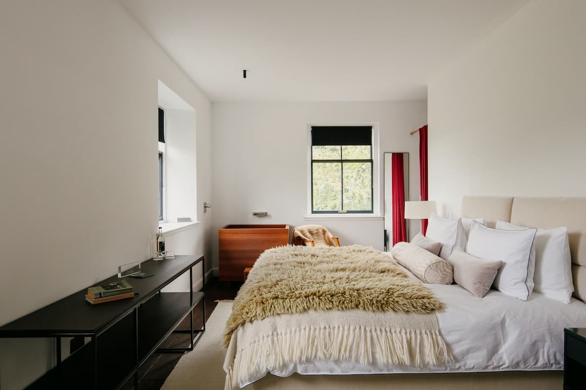 A bedroom with a bed, a nightstand, a dresser, a window, and a mirror.