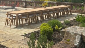 An outdoor dining area with a long wooden table and chairs, surrounded by a stone railing, overlooking a lush green landscape with hills. - Dun Aluinn  (Aberfeldy)