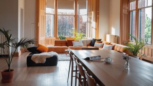 A room with a wooden dining table, a sofa set, and large windows with a view of trees. - Dun Aluinn  (Aberfeldy)