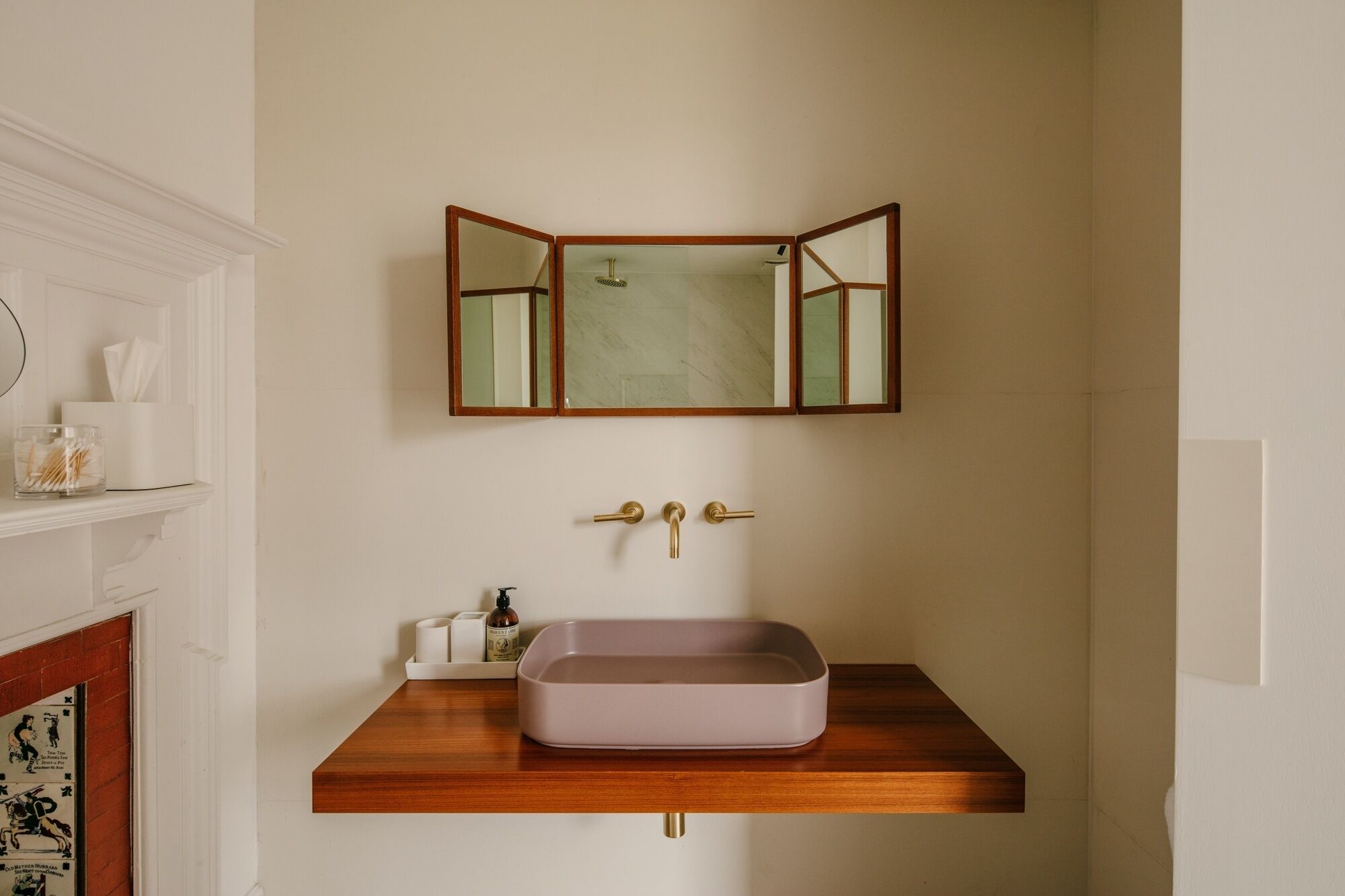 A bathroom with a wooden vanity, a rectangular sink, and a mirror with a wooden frame.