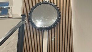 A staircase with a wooden panel wall, a round mirror, and a black railing. - WORLD CUP READY :- Cozy 1-bedroom modern luxury loft (Harrison)
