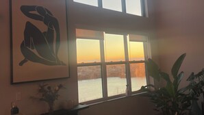 A room with a large window, a framed artwork, a plant, and a sofa with cushions. - WORLD CUP READY :- Cozy 1-bedroom modern luxury loft (Harrison)