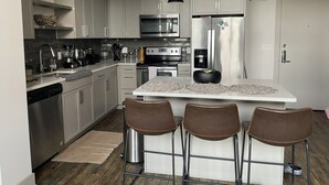A modern kitchen with stainless steel appliances, a central island with bar stools, and pendant lighting. - WORLD CUP READY :- Cozy 1-bedroom modern luxury loft (Harrison)