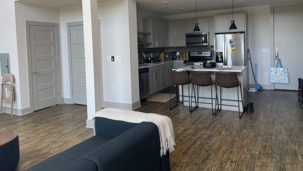 A modern kitchen with stainless steel appliances, a dining area with bar stools, and a living room with a dark-colored sofa. - WORLD CUP READY :- Cozy 1-bedroom modern luxury loft (Harrison)
