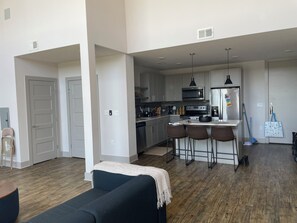 A modern kitchen with stainless steel appliances, a dining area with bar stools, and a living room with a dark-colored sofa. - WORLD CUP READY :- Cozy 1-bedroom modern luxury loft (Harrison)