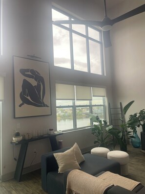 A modern living room with a large window, a sofa, a coffee table, and a painting. - WORLD CUP READY :- Cozy 1-bedroom modern luxury loft (Harrison)