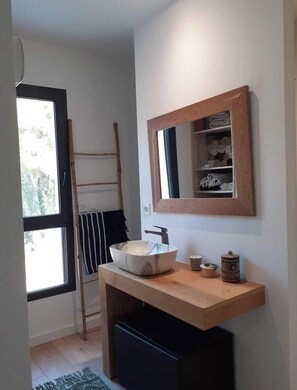Ein modernes Badezimmer mit einem Holzkosmetikschrank, einem großen Spiegel und einem Fenster mit Blick auf Bäume.