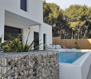 Ein modernes Haus mit Swimmingpool, Holzzaun und Blick auf Bäume.
