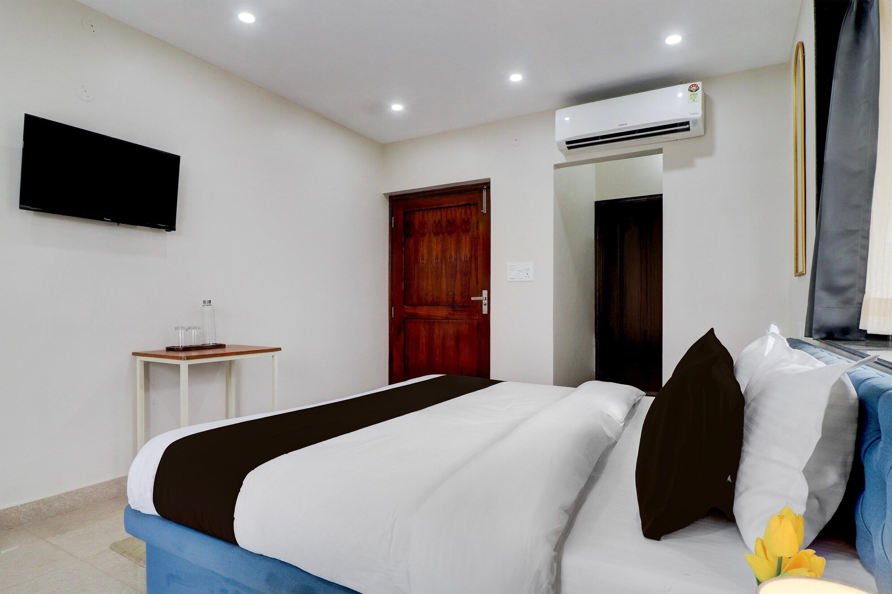 Une chambre d’hôtel avec un lit, une télévision, un climatiseur, une porte en bois et une petite table.