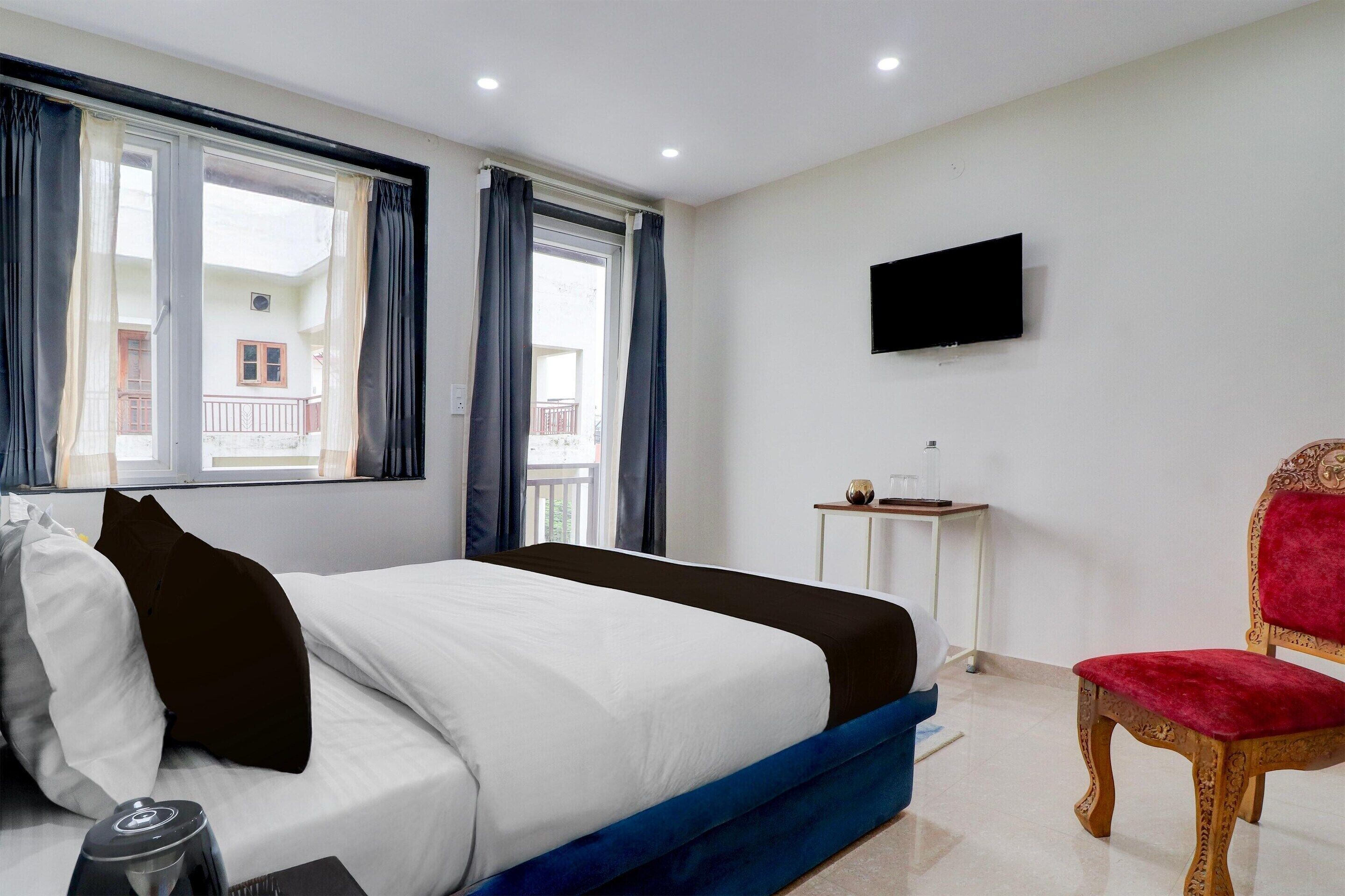 A hotel room with a bed, a television mounted on the wall, a chair, and a window with curtains.