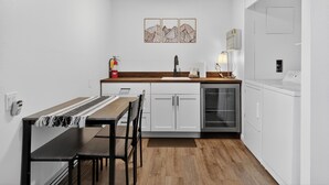 Une cuisine compacte dotée d’un plan de travail en bois, de meubles blancs, d’un lave-vaisselle encastré et d’un coin repas avec une table et des chaises.