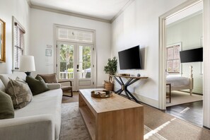 Un salon bien éclairé, avec un canapé, une table basse, un téléviseur et une porte donnant sur un balcon.