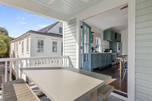 Un espacio al aire libre techado con una mesa y sillas, vista a una casa, y una cocina con gabinetes color turquesa.