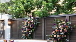 Un espace extérieur aménagé avec une table en verre, des bancs rembourrés et des compositions florales.