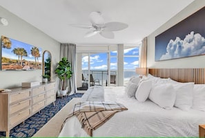 Ein Hotelzimmer mit Bett, Deckenventilator, großem Fenster mit Aussicht, Kommode und Spiegel.