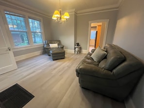A living room with a leather sofa, a recliner, a small table with a dog statue, and a chandelier.