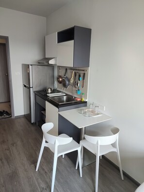 Een kleine keuken met een koelkast, fornuis, spoelbak en twee witte stoelen.