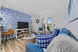 Ein Wohnzimmer mit Fernseher, eine Essecke mit Tisch und Stühlen sowie einer Wand mit Muster.