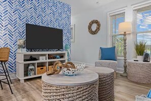 Ein Wohnzimmer mit Fernseher, Korbsesseln, einer weißen Ablage und einer blauen Wand mit Muster.