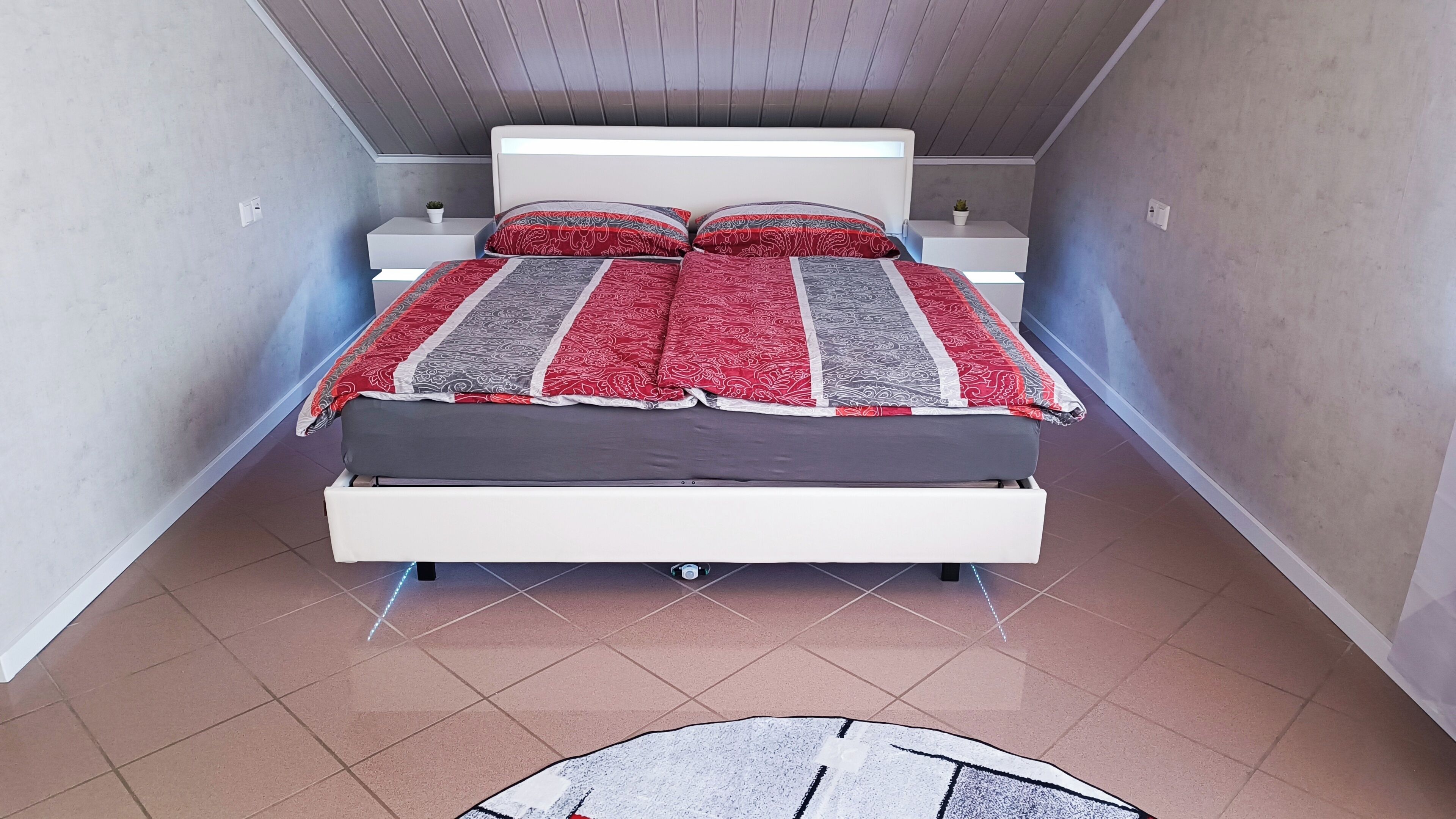 Une petite pièce étroite comprenant un lit, une petite table et une plante en pot.